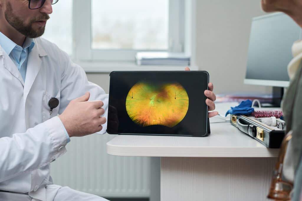 Ophthalmologist explaining an eye condition to a patient using tablet with retina scan